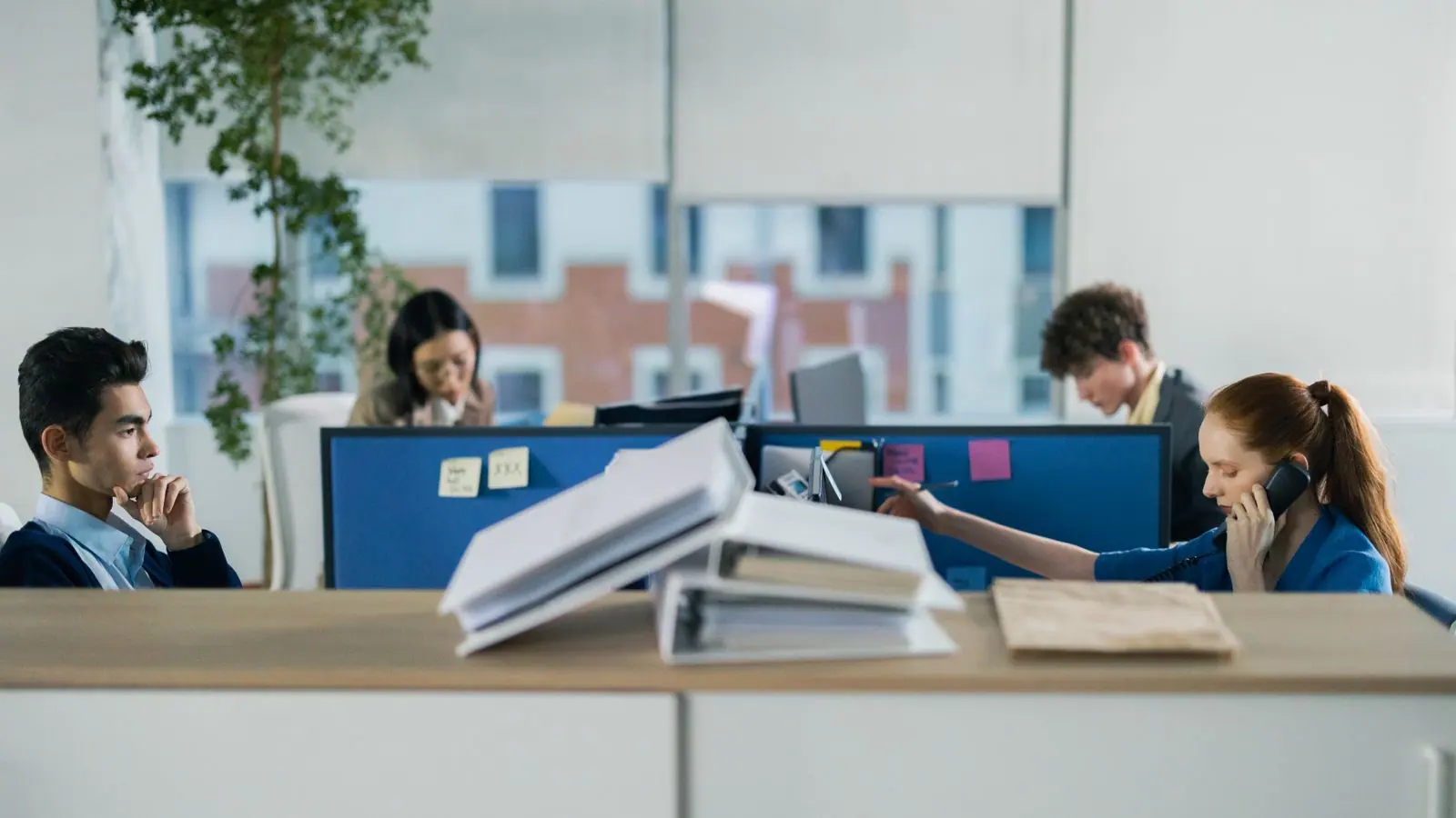 Personas trabajando en una oficina abierta con carpetas sobre el mostrador